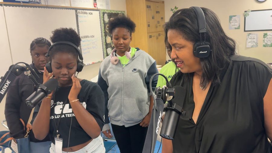 Teens in Boys & Girls Club shirts gather around a boom-arm microphone. One holds her headphones to her ear while a facilitator in headphones talks with them.